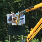 SBD workers install sign face from lift. Lift work